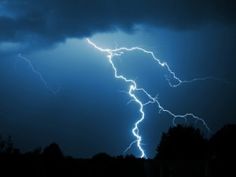 a lightning bolt is seen in the sky above some trees and grass, with dark clouds behind it