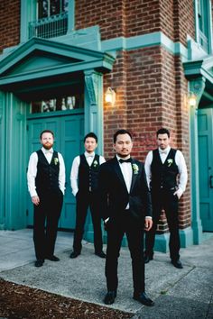 a group of men standing next to each other in front of a green brick building