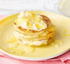 a stack of pancakes topped with butter and syrup on a yellow plate next to a glass of milk