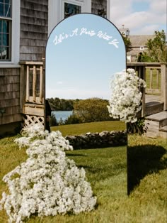 a mirror sitting on top of a grass covered field next to a building and flowers