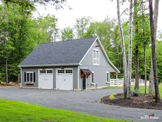 a gray garage with two doors on the front and side of it, surrounded by trees