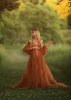 a woman in an orange dress is standing in the grass with her hands out and looking off into the distance