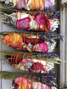 several bundles of dried flowers tied together with orange and purple string on them, sitting in front of a white wall