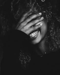 a woman with curly hair smiling and holding her hands to her face