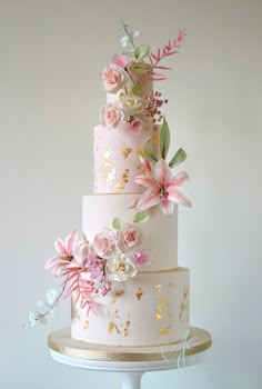 a three tiered wedding cake with pink flowers on the top and gold trimmings