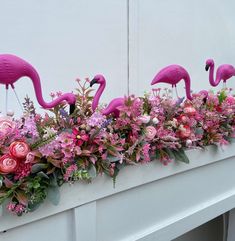 three pink flamingos sitting on top of a window sill filled with flowers and greenery