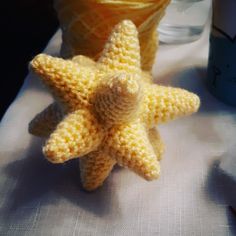 a crocheted yellow starfish next to a cup of water on a table