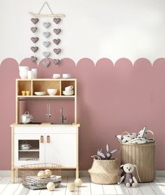 a white and pink play kitchen in a room with hearts on the wall above it