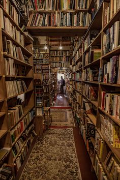 a narrow bookshelf filled with lots of books and people standing in the doorway