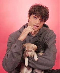 a young man holding two puppies in his arms and looking at the camera while sitting down