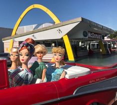 three barbie dolls sitting in the back of a red car with a mcdonald's sign