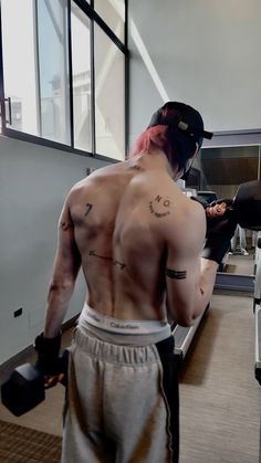 a man with pink hair and tattoos on his back is in a gym holding dumbbells