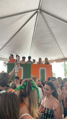 a group of people standing under a white tent at a music festival, some holding up their cell phones