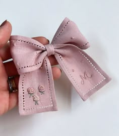 a hand holding a small pink bow with embroidered flowers on the front and side of it