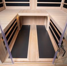 the inside of a wooden sauna with glass doors and black mats on the floor