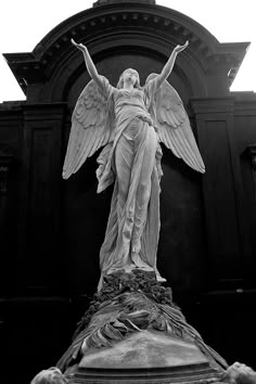 an angel statue stands in front of a black and white building with its arms outstretched