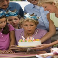 an older woman blowing out candles on a birthday cake with her granddaughter and two younger children