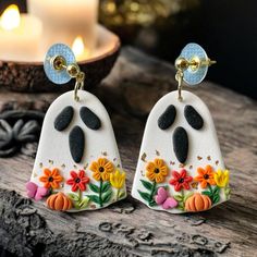 a pair of white and black earrings with flowers painted on the front, sitting on a wooden table next to a lit candle