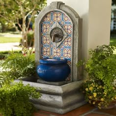 a fountain with a blue pot on top of it next to some plants and trees