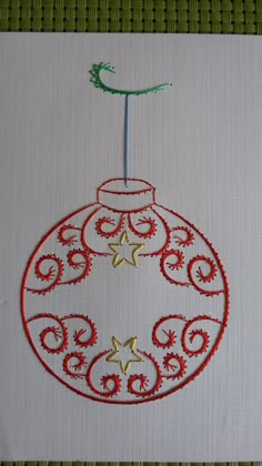 a christmas ornament is shown on a white piece of paper with red thread