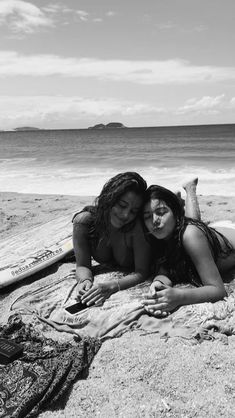 two women laying on top of a beach next to the ocean