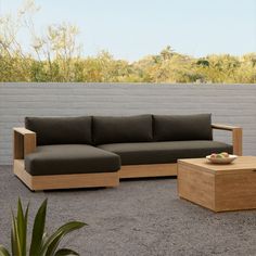 a couch sitting on top of a cement floor next to a wooden table and potted plant