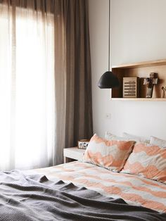 a bed sitting under a window next to a wooden shelf