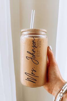 a person holding a mason jar with a straw in it and writing on the side