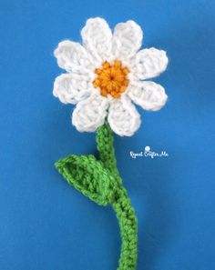 a crocheted white flower with green stems on a blue background, ready to be made into a brooch or pin