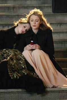 two women sitting on steps looking at their cell phones