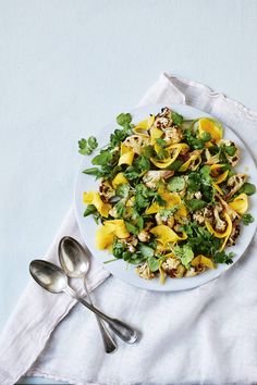 a white plate topped with pasta and veggies on top of a table next to two silver spoons