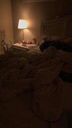 an unmade bed in a dimly lit room with a lamp on the side table