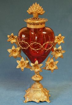 a red vase sitting on top of a table next to a golden flower decoration stand