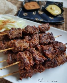 several skewered meats are sitting on a white plate