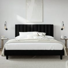 a bed with white sheets and black headboard in a room next to two tables