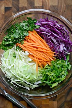 chopped vegetables in a glass bowl on top of a wooden table next to utensils