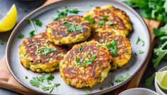 three crab cakes on a plate with cilantro and limes next to it