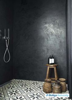 a bathroom with black walls and white tile flooring, two wooden stools in front of the shower