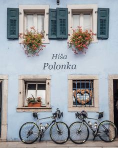 three bicycles parked in front of a blue building with windows and shutters on the side