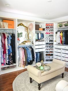 an organized closet with white furniture and lots of clothes on shelves in the middle of it