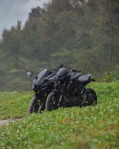 two motorcycles parked on the side of a dirt road in front of green grass and trees