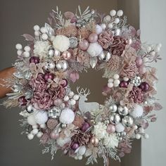 a hand holding a christmas wreath with pink and white decorations on it's front door