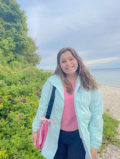 a girl standing on the beach with her hand in her pocket and smiling at the camera