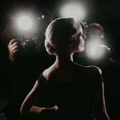 a woman standing in front of a group of people with lights on her head and hands behind her back