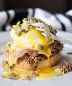 a white plate topped with meat and cheese covered in sauce next to a fork on top of it