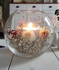 a glass bowl filled with flowers and a lit candle on top of a white table