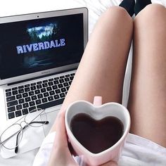 a woman is holding a heart shaped coffee cup in front of her laptop