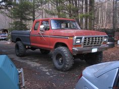 an old red pick up truck parked in the woods