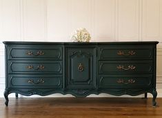 a black dresser with gold handles and flowers on top is shown in front of a white wall