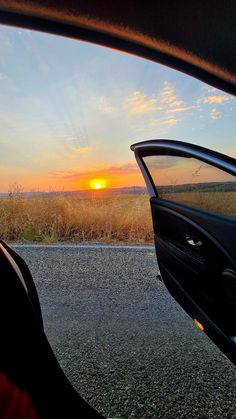 the sun is setting over an open field as seen from inside a car's side view mirror